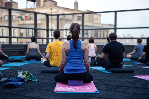 A group of 20 and 30 somethigns sit in a yoga pose on the roof